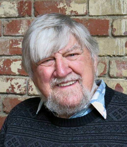Headshot of Dick looking into the camera and smiling. He has facial hair and is in front of a brick wall.