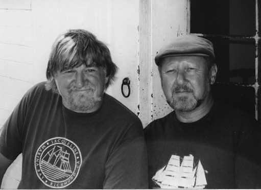 A photo of Holdstock and MacLeod. Black and white image of two men looking at the camera, both with beards, one is wearing a hat.