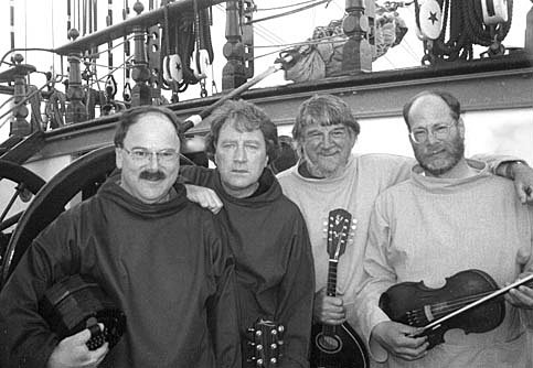 Black and white image of 4 men on a ship looking at the camera. They are all holding musical instruments.